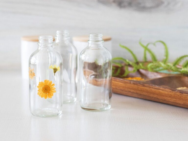 glass bottles next a tray of pressed flowers on light counter